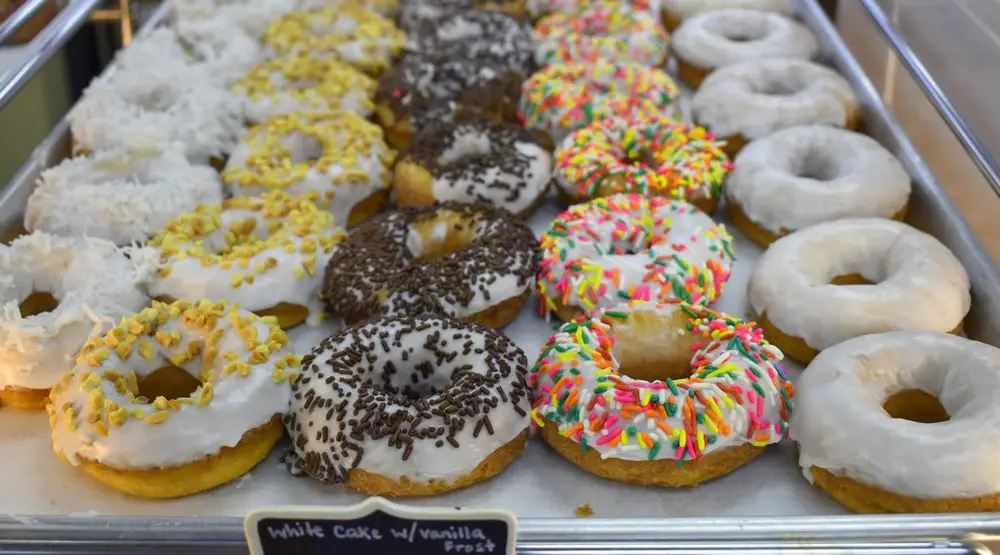 A delightful tray of assorted donuts awaits, adorned with coconut, nuts, sprinkles, and chocolate shavings—perfect for celebrating National Donut Day in style.