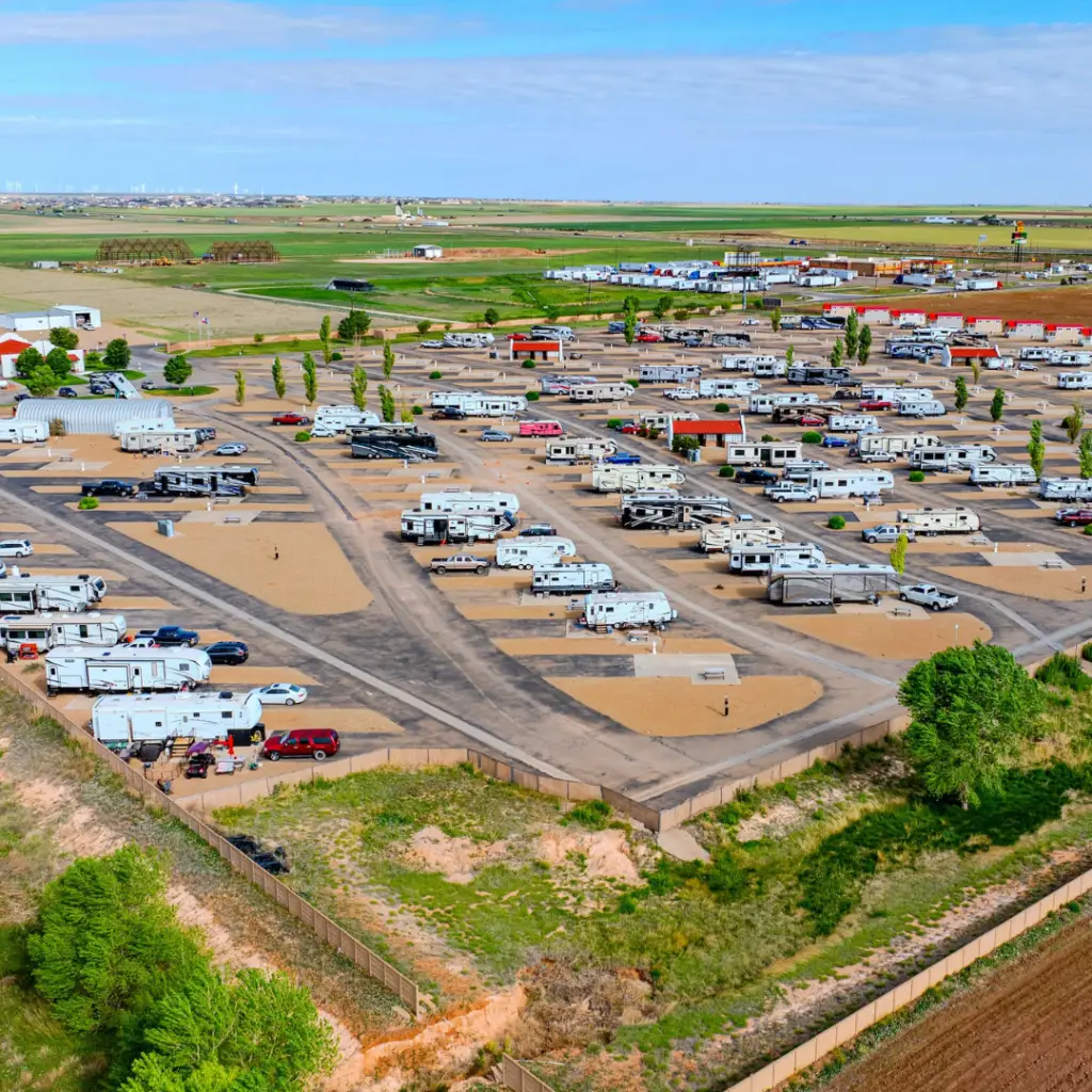 Aerial view of a sprawling RV park along I-40, showcasing numerous vehicles and trailers in designated spots. This popular RV overnight stop is surrounded by greenery and open fields under a partly cloudy sky, creating a serene escape for travelers.