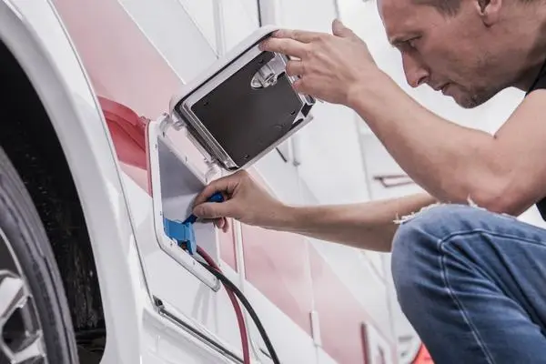 Person diligently plugging a blue cable into the camper van's external charging port, a key step in RV maintenance for trip preparation.