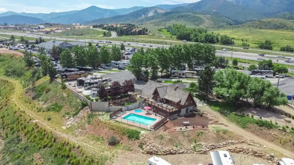 Aerial view of a charming rural property featuring a house, swimming pool, and several RVs nestled near Park City. A highway threads through the landscape as majestic mountains rise in the background.