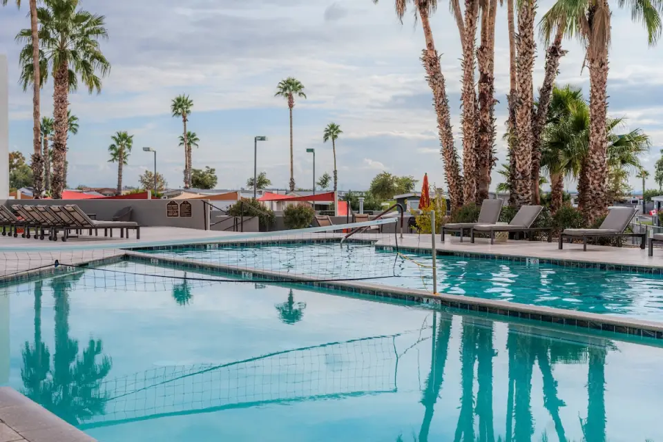 At the Gold Canyon RV Resort, enjoy the outdoor swimming pool surrounded by lounge chairs and palm trees, with a volleyball net ready for play. Perfect for a winter getaway, even under an overcast sky.