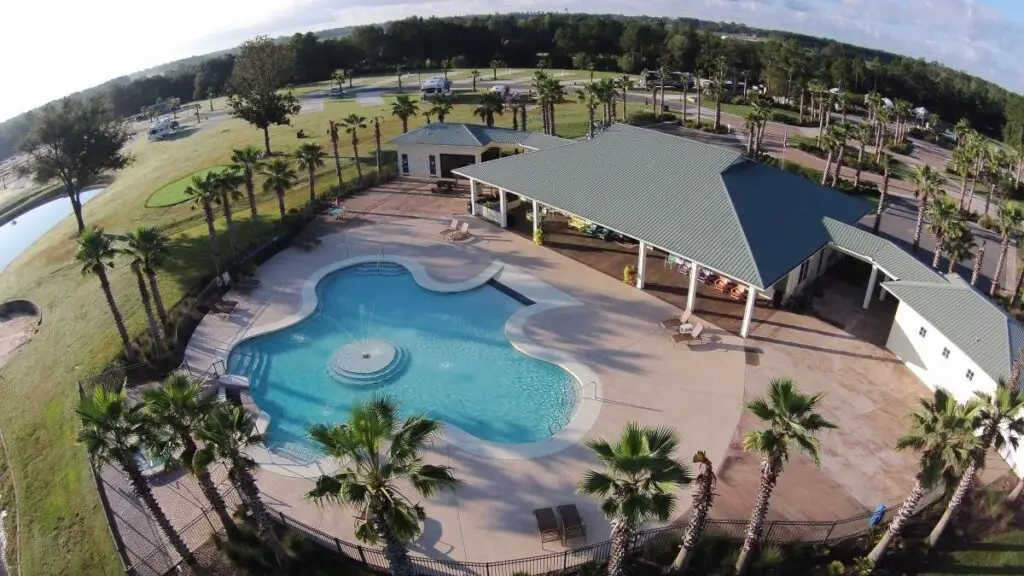 Aerial view of a swimming pool surrounded by palm trees, with adjacent buildings and a parking area near the serene waters of Lake Osprey in the background.