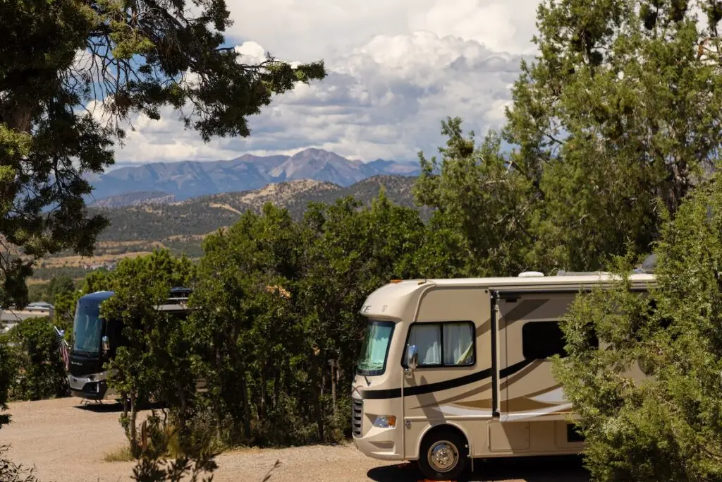 Two RVs parked among trees create a serene oasis at Durango, framed by a majestic mountainous landscape under a cloudy sky.
