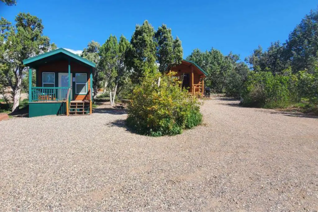 Two cozy cabins nestle among trees on a gravel path under a clear blue sky, offering a serene retreat at Durango Resort.
