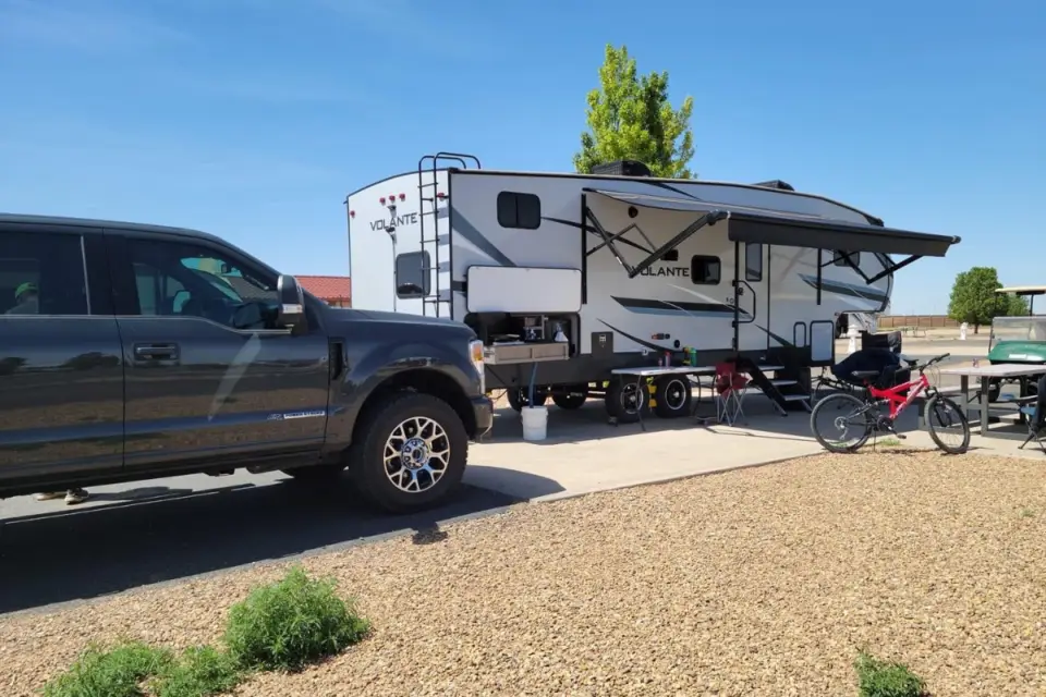 A pickup truck is parked next to a white Volante RV on one of Amarillo's premium RV sites, complete with an extended awning and a bike resting outside on the gravel surface.