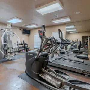 The gym room at Rayford Crossing features treadmills, elliptical machines, a weight machine, and dumbbells. All equipment is neatly arranged with mirrors lining the walls for an optimal workout experience.