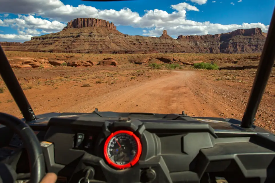 A person embarks on an adventurous drive through the desert landscape, navigating a dirt road between majestic mesas and under a clear blue sky, perhaps celebrating Father's Day by exploring the rugged beauty near Arches National Park.