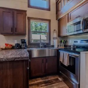 This compact modern kitchen, perfect for vacation rentals, features dark wood cabinets, stainless-steel appliances, and a sleek marble countertop. A small window brightens the space where a basket and coffee maker rest invitingly on the counter.