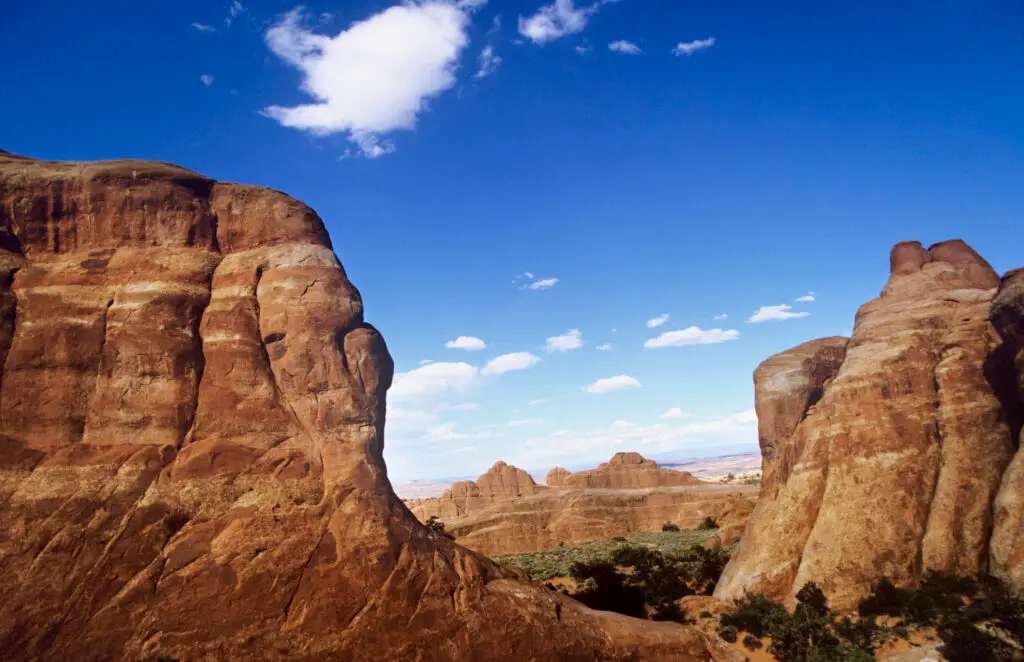A scenic view of a desert landscape, reminiscent of those found in National Parks, with large red rock formations and a clear blue sky dotted with scattered clouds. Perfect for exploring on Free Entrance Days in 2022.