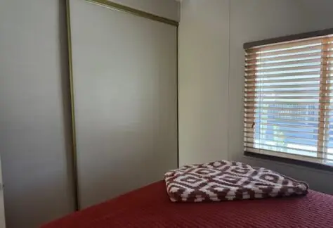 The Parkwest bedroom features a red bedspread, a patterned blanket, wooden blinds adorning the window, and closed sliding closet doors. A great real estate opportunity awaits with this charming space now available at a reduced price.