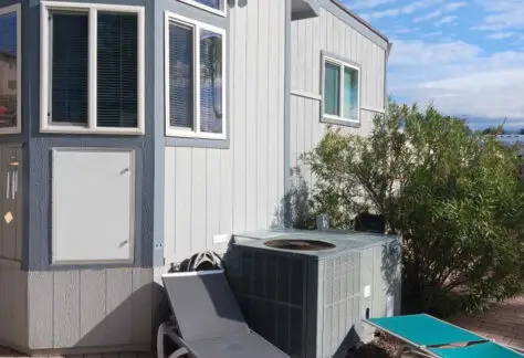 A 2010 Chariot Eagle house with large windows and a sloped roof, equipped with an air conditioning unit outside and two lounge chairs on a cozy brick patio.