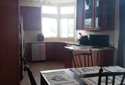 A cozy mobile home kitchen features wooden cabinets, a dining table with placemats, a vintage chandelier, and a computer on the counter. This charming space, reminiscent of Chariot Eagle's 2010 designs, blends functionality and style seamlessly.