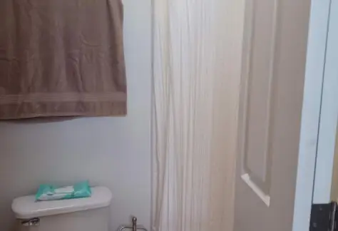 A compact RV bathroom with a toilet, toilet paper holder, and shower area features a towel hanging above the toilet. A pack of wipes sits on the tank lid. The 2010 Chariot Eagle model is complete with a shower adorned by a simple white curtain.