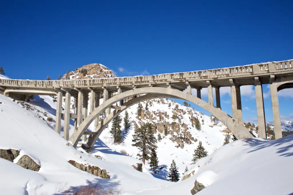 A concrete arch bridge gracefully spans the snowy landscape of Truckee, California. With the clear blue sky and rocky hills in the background, this spot is a perfect highlight for scenic winter drives.