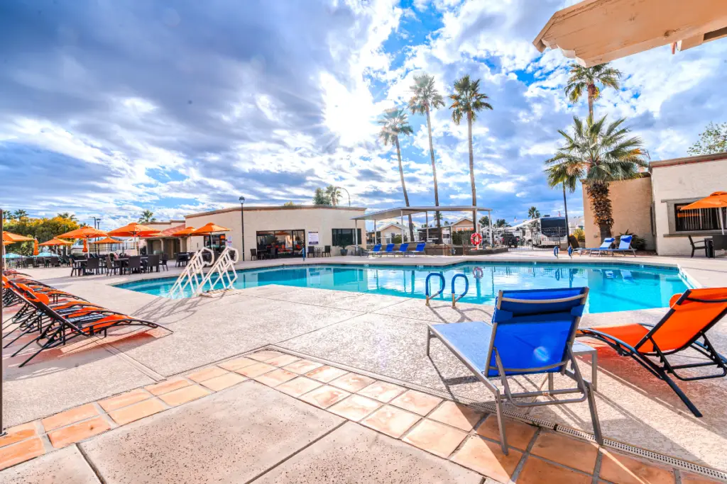The outdoor pool area, with its lounge chairs and umbrellas, offers a perfect retreat under the palm trees. As the countdown to sunrise begins under a partly cloudy sky, secure your spot for a serene morning experience.