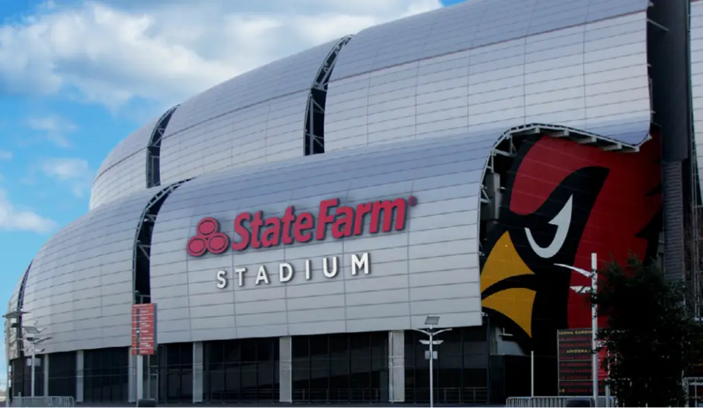 State Farm Stadium exterior, showcasing a partial view of a cardinal emblem, stands proudly amidst the natural beauty of Arizona. Nearby, the Pueblo El Mirage RV Resort offers an inviting glimpse into local culture and leisure.