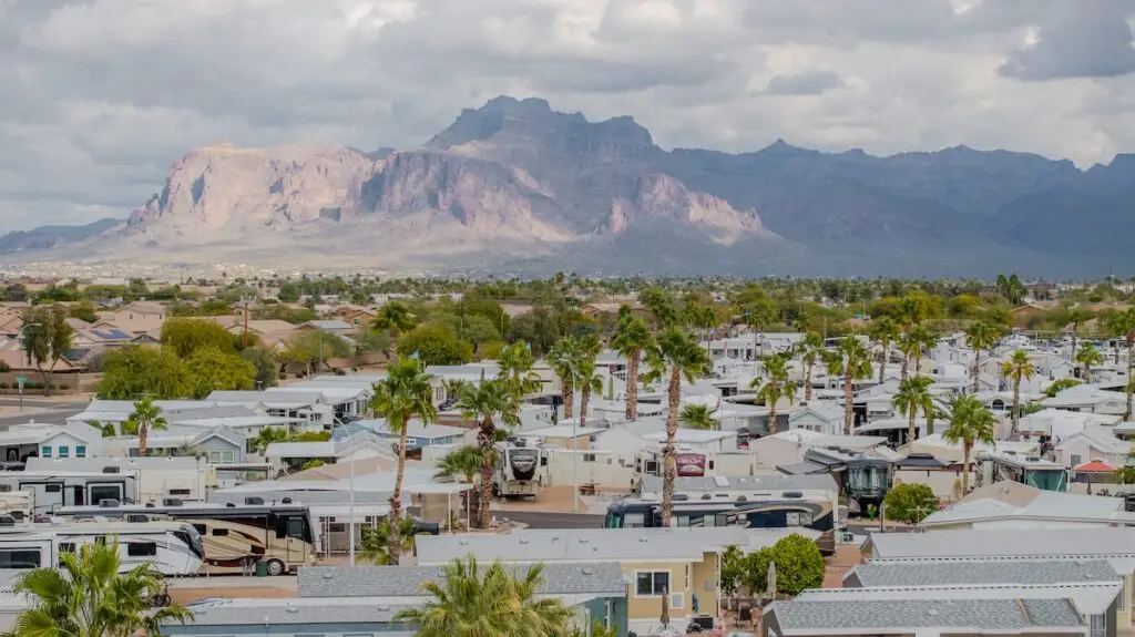 Aerial view of a cozy retirement community with trailers and palm trees, all nestled against a backdrop of mountains under cloudy skies. Perfect for planning ahead, this picturesque setting invites you to consider your ideal winter stay.