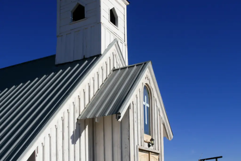 A white wooden church with a small belfry and a cross on the front stands proudly under the clear blue sky, capturing the essence of local culture amid natural beauty.