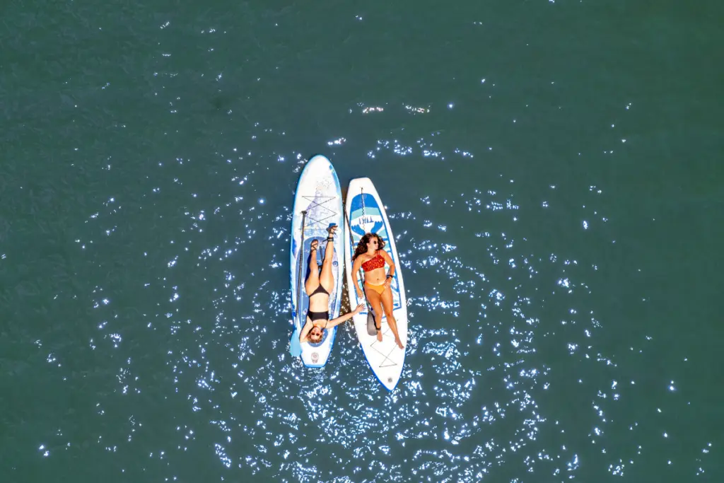 Two people relax on paddleboards in Lake Conroe, with sunlight reflecting off the surface, just a stone's throw from the rustic cabins of Water's Edge Resort.