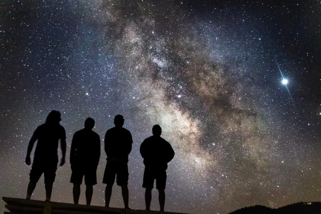 Four silhouetted figures stand against a starry sky with the Milky Way visible above them, capturing a serene moment in Moab, Utah. It's as if the universe itself is joining their New Year's celebration under the cosmic tapestry.