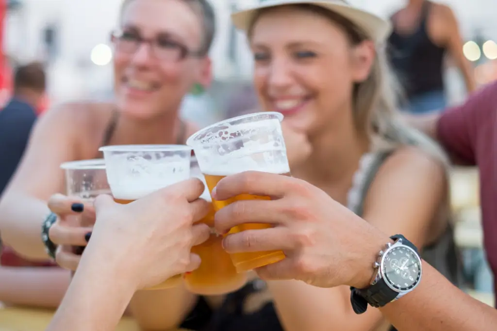 At the Coachland RV Resort in Truckee, four people clink plastic cups of beer together, smiling and sitting at a wooden table outdoors, savoring the spirit of summer events.