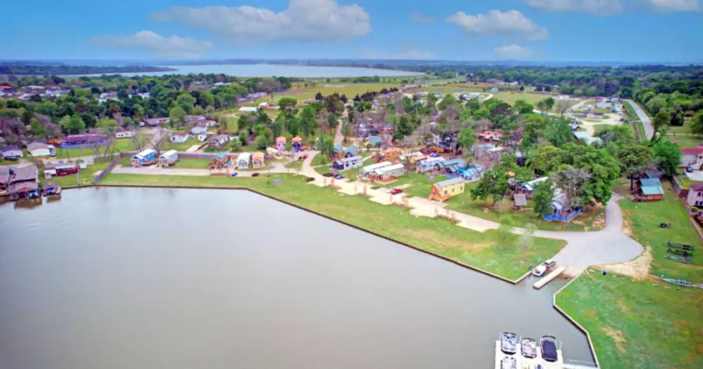 Aerial view of a lakeside residential area with houses, greenery, and a dock at Lake Conroe. Ideal for a vacation rental, the lake stretches across the foreground beneath a cloudy sky.