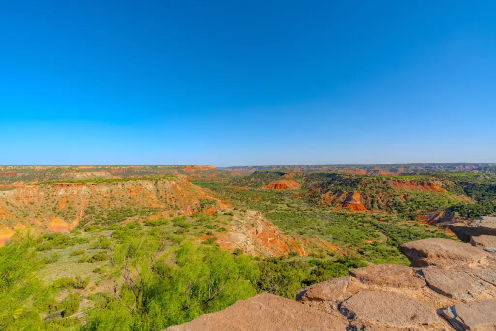 Experience the vast landscape of a canyon with stunning red rock formations, lush green vegetation, and a clear blue sky—perfect for your summer adventure ideas in Amarillo.