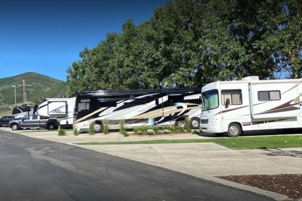 Several RVs are parked alongside a road, embraced by the enchanting allure of Spring's Magic. With trees and a small hill painting the backdrop on a clear day, this scene exudes the peaceful charm you'd expect from an idyllic RV resort.