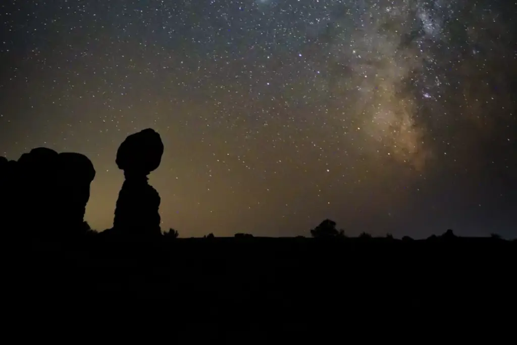 Experience a unique night in Moab as the silhouette of Balanced Rock stands majestically against a starry sky, with the Milky Way painting a breathtaking backdrop.