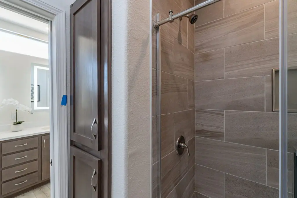 Modern bathroom featuring a tiled shower with a glass door, wooden cabinets, and a vanity with a sink and mirror in the background.
