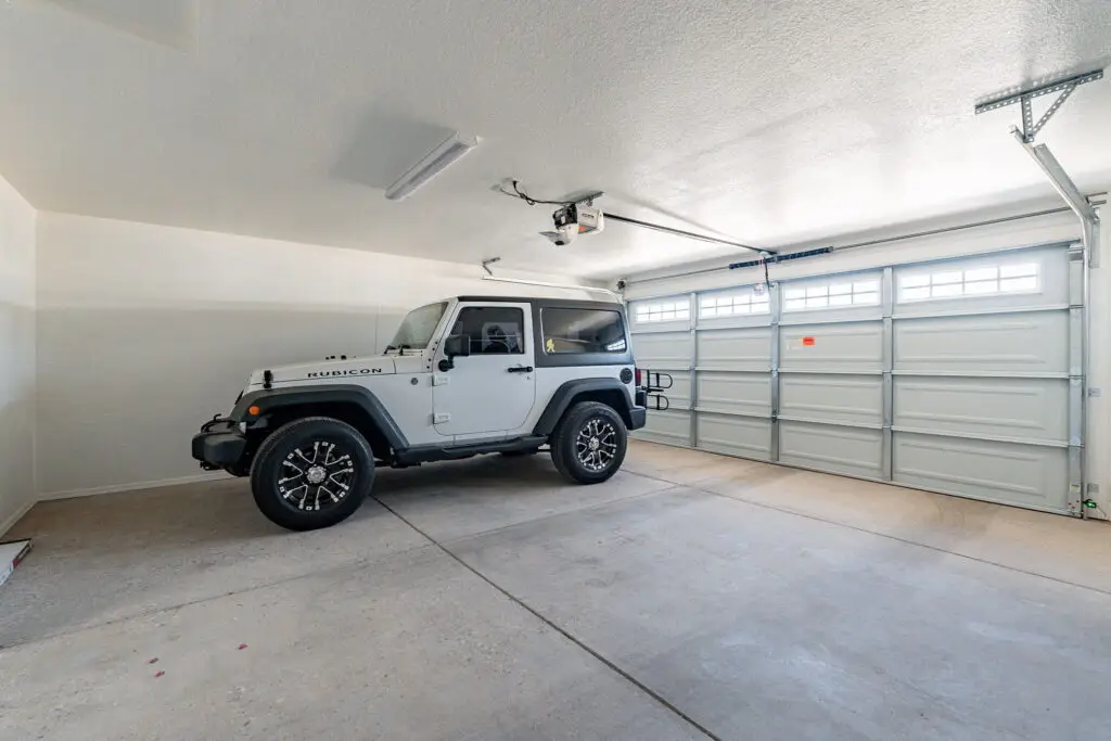 A white Jeep is parked inside a clean, empty two-car garage with closed doors.