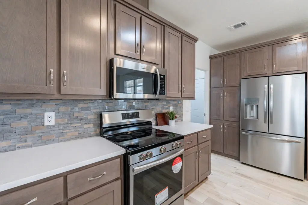 Modern kitchen with stainless steel appliances, including a stove, microwave, and refrigerator, and gray wood cabinets with a tile backsplash.