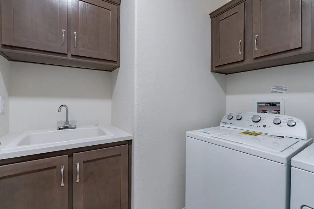 Laundry room with a sink, brown cabinets, and a white washing machine against a light-colored wall.