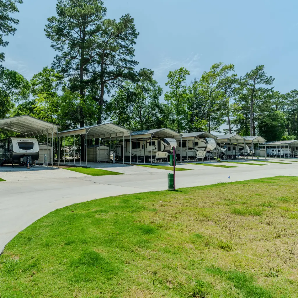 A row of RVs parked under metal shelters in Majestic Pines campground, surrounded by trees and greenery on a sunny day, offers an idyllic setting for Winter Texan RV Living enthusiasts seeking monthly stay options.