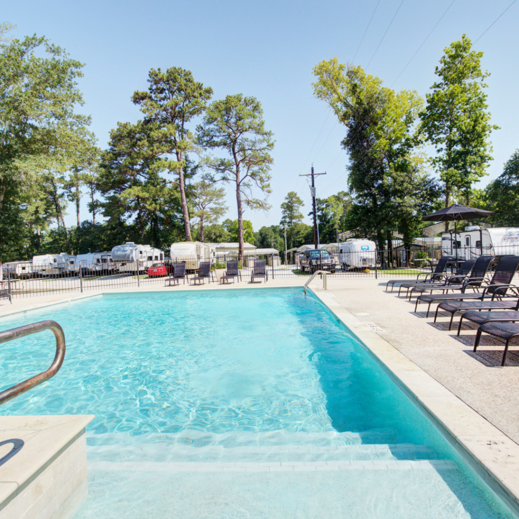 The outdoor swimming pool, framed by majestic pines and RV spots in the background, features lounge chairs on the right, offering a tranquil retreat with easy access to nature.