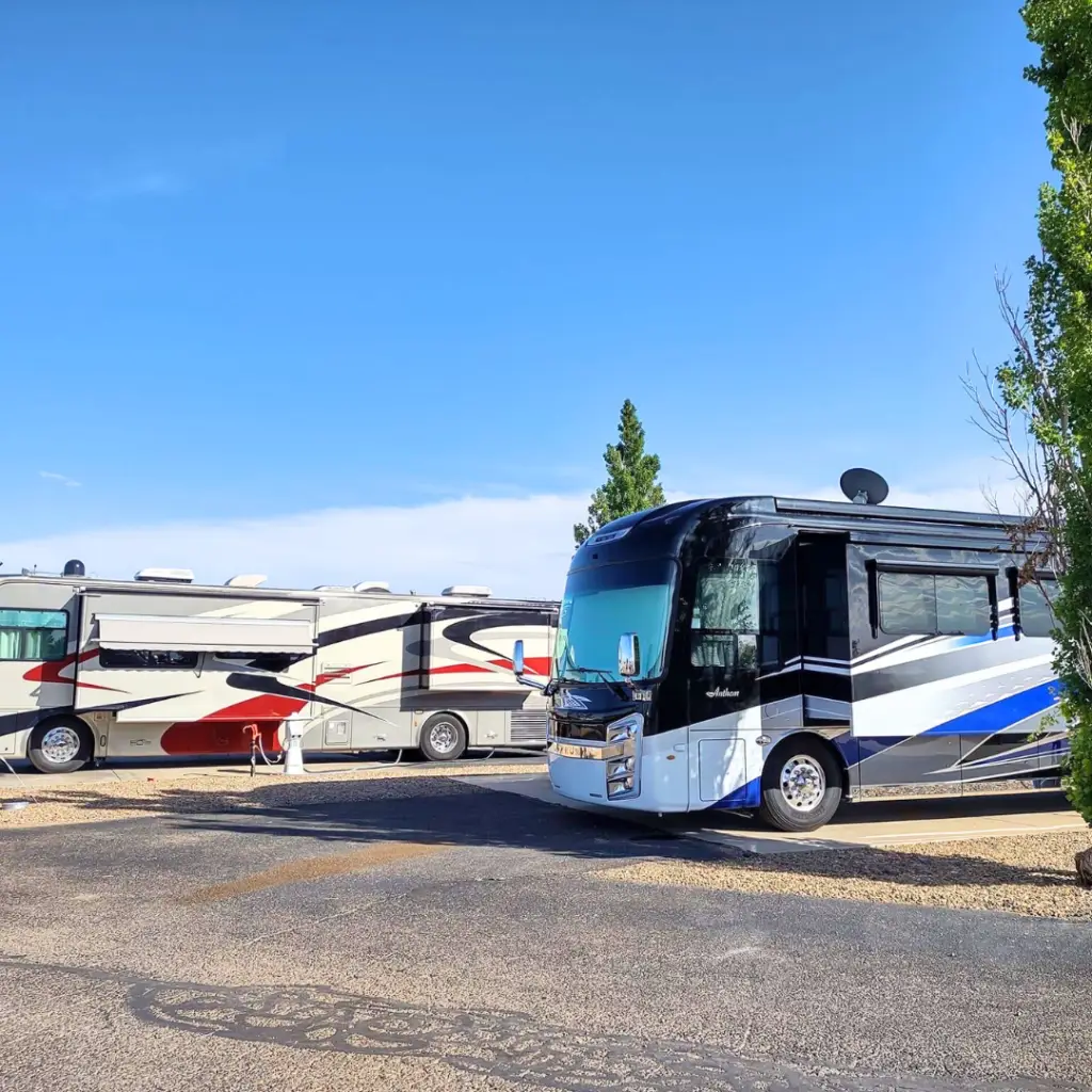 Two large RVs parked on a paved area under the clear blue Amarillo sky, with trees in the background, hint at a seasonal stay ready for thrilling adventure.