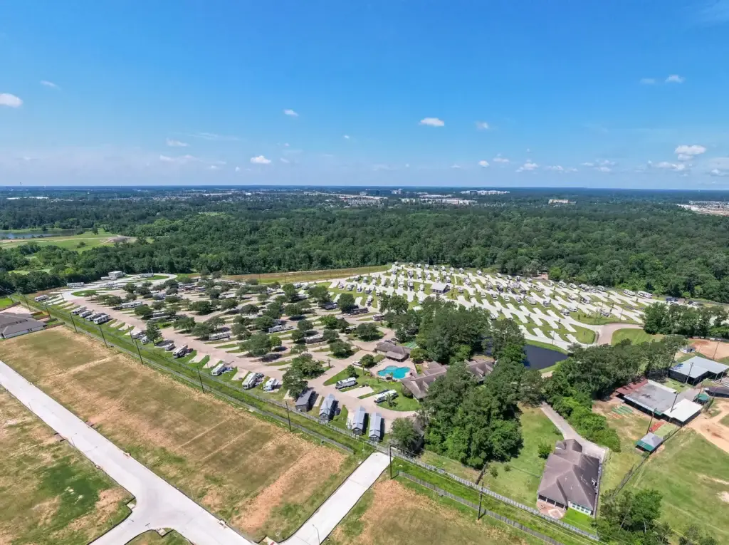Aerial view of an RV park with rows of recreational vehicles nestled among greenery, just a short drive from the Houston Rodeo, under a clear blue sky.
