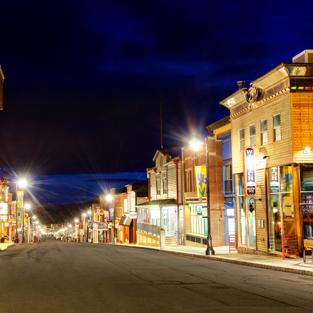 A quiet, brightly lit street at night in Park City showcases colorful, historic-style buildings with various signs and facades, offering a charming backdrop for a Spring RV Escape.