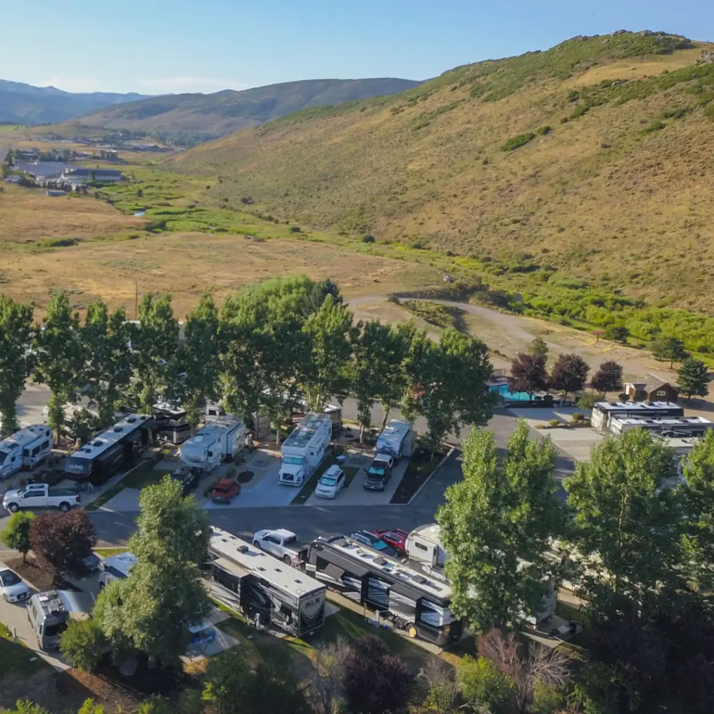 Aerial view of Park City RV Resort, where several RVs are nestled among trees, set against rolling hills under a clear blue sky. This perfect spot for an RV stay offers breathtaking views and serenity, making it an ideal getaway to ring in the New Year.