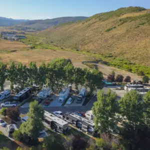 Aerial view of Park City RV Resort, where several RVs are nestled among trees, set against rolling hills under a clear blue sky. This perfect spot for an RV stay offers breathtaking views and serenity, making it an ideal getaway to ring in the New Year.