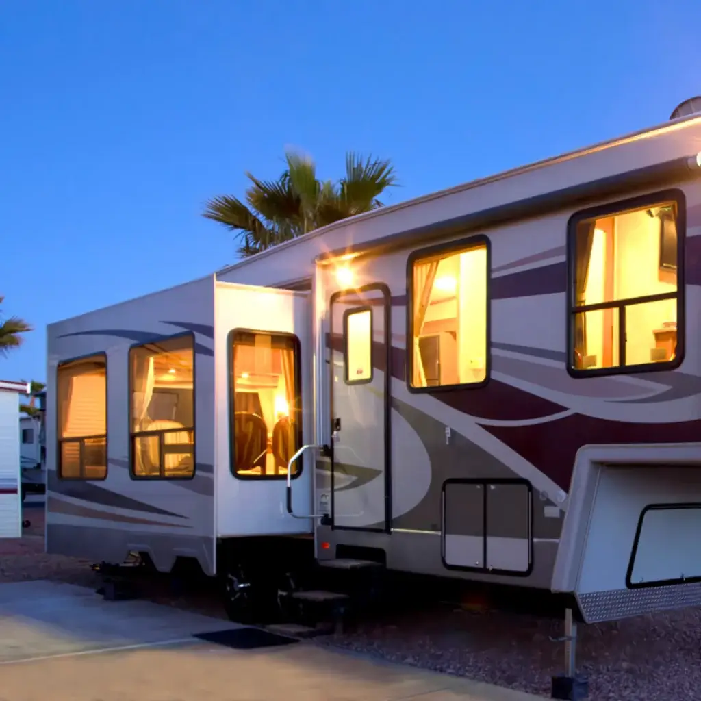 A modern RV is securely parked on a paved site, its interior lights warmly glowing, surrounded by swaying palm trees at dusk—a perfect haven for winter visitors.