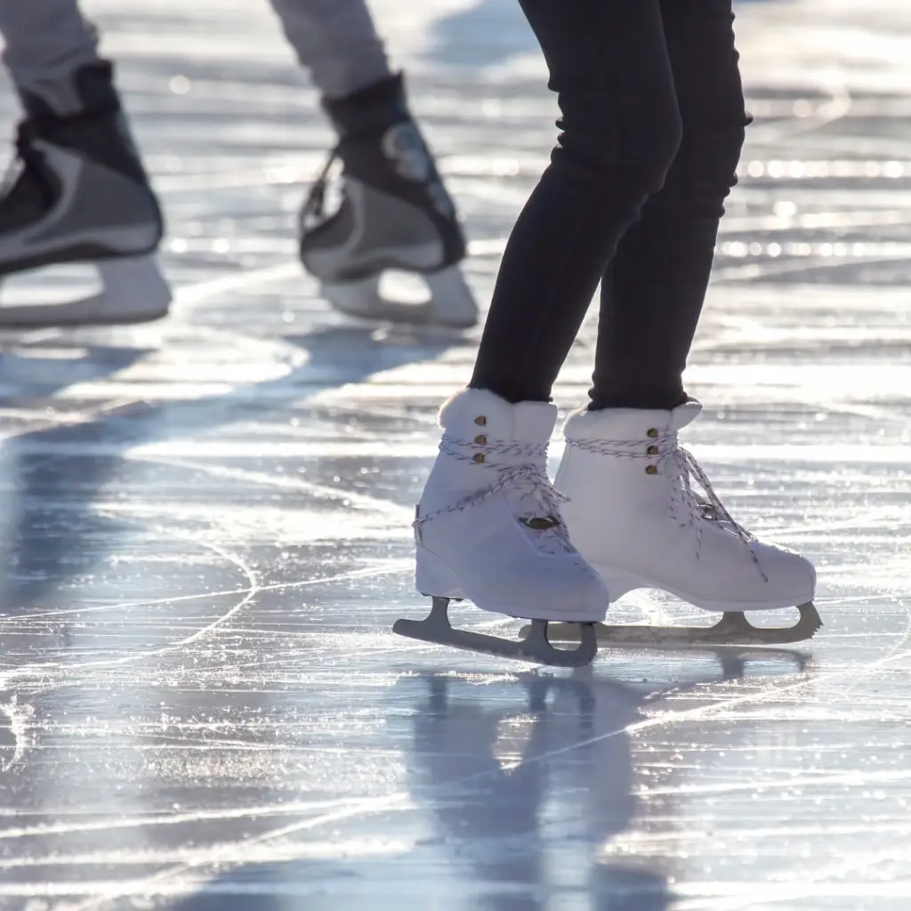People ice skating on a reflective rink, wearing white and gray skates, in the heart of Park City's winter adventure.