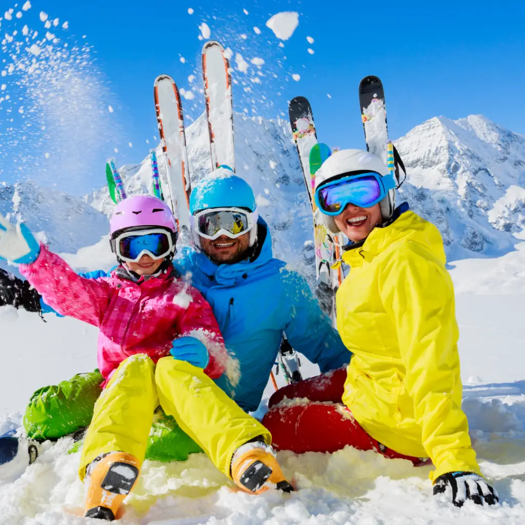 A group of skiers in colorful gear sits cheerfully in the snow with the majestic mountains of Park City in the background, embracing the thrill of winter skiing adventures.