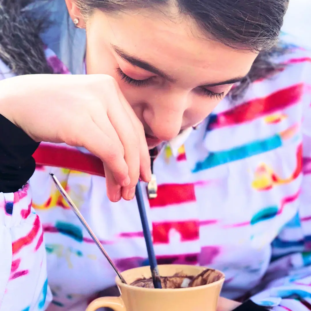 In Park City, a person in a colorful jacket enjoys a warm mug with a spoon, savoring the moment after a day of winter skiing adventures.