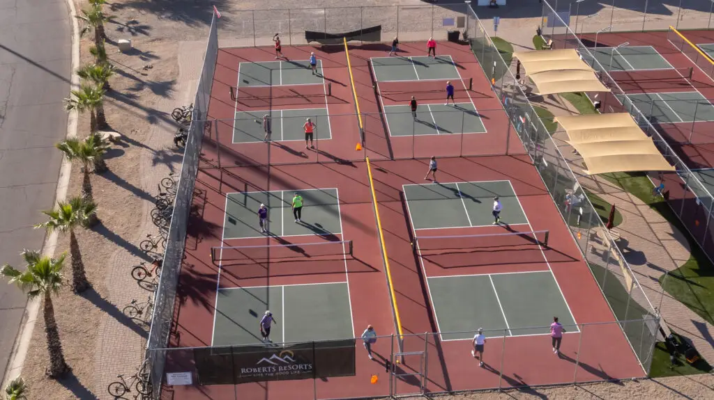 Aerial view of people enjoying pickleball at Pueblo El Mirage in January, with multiple outdoor courts surrounded by fences and shaded areas under clear skies.