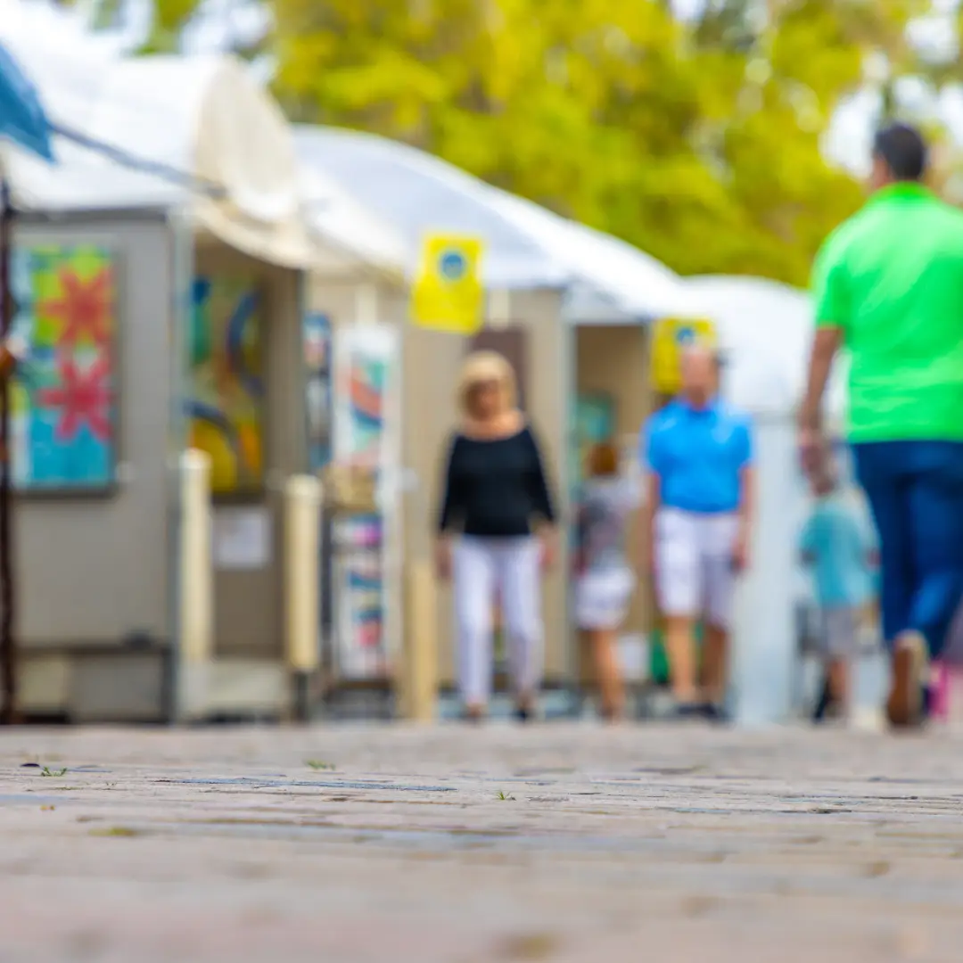 A walkway lined with art tents and colorful paintings captures the essence of downtown charm. As people stroll along the path, surrounded by blossoming trees, they embrace the vibrant spirit of spring in Park City.