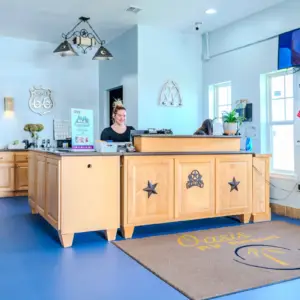 Reception area with a smiling receptionist behind a wooden desk. Signs and decor are on the walls, and a "Good Sam Park" sign is displayed. A TV is mounted above.