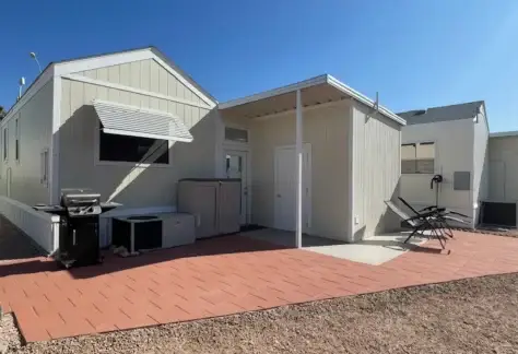 Lot 430 features a charming, small Cavco building from 2013. It has a light-colored exterior with a covered entrance and an air conditioning unit. Outside, enjoy grilling on the red tiled patio under the clear blue sky.