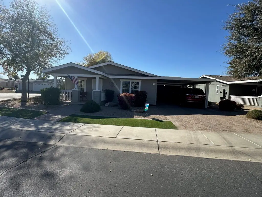 Single-story house with a carport, American flag, and landscaped yard, under a clear blue sky.