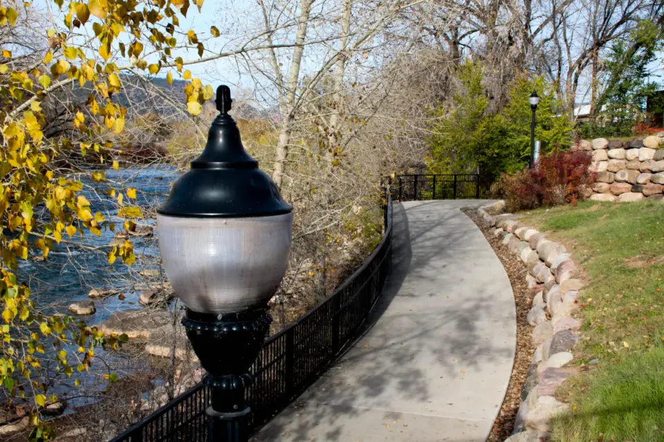 Stroll along the paved walkway in Durango, where a vintage streetlamp graces your path. Surrounded by autumn trees with a river on the left and a stone wall bordering a grassy area on the right, this serene escape offers an ultimate guide to seasonal charm and spring adventures.